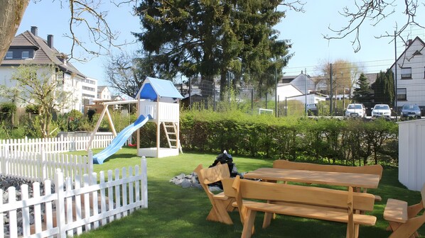 A playground with a slide and swings, a picnic table, and a white picket fence.