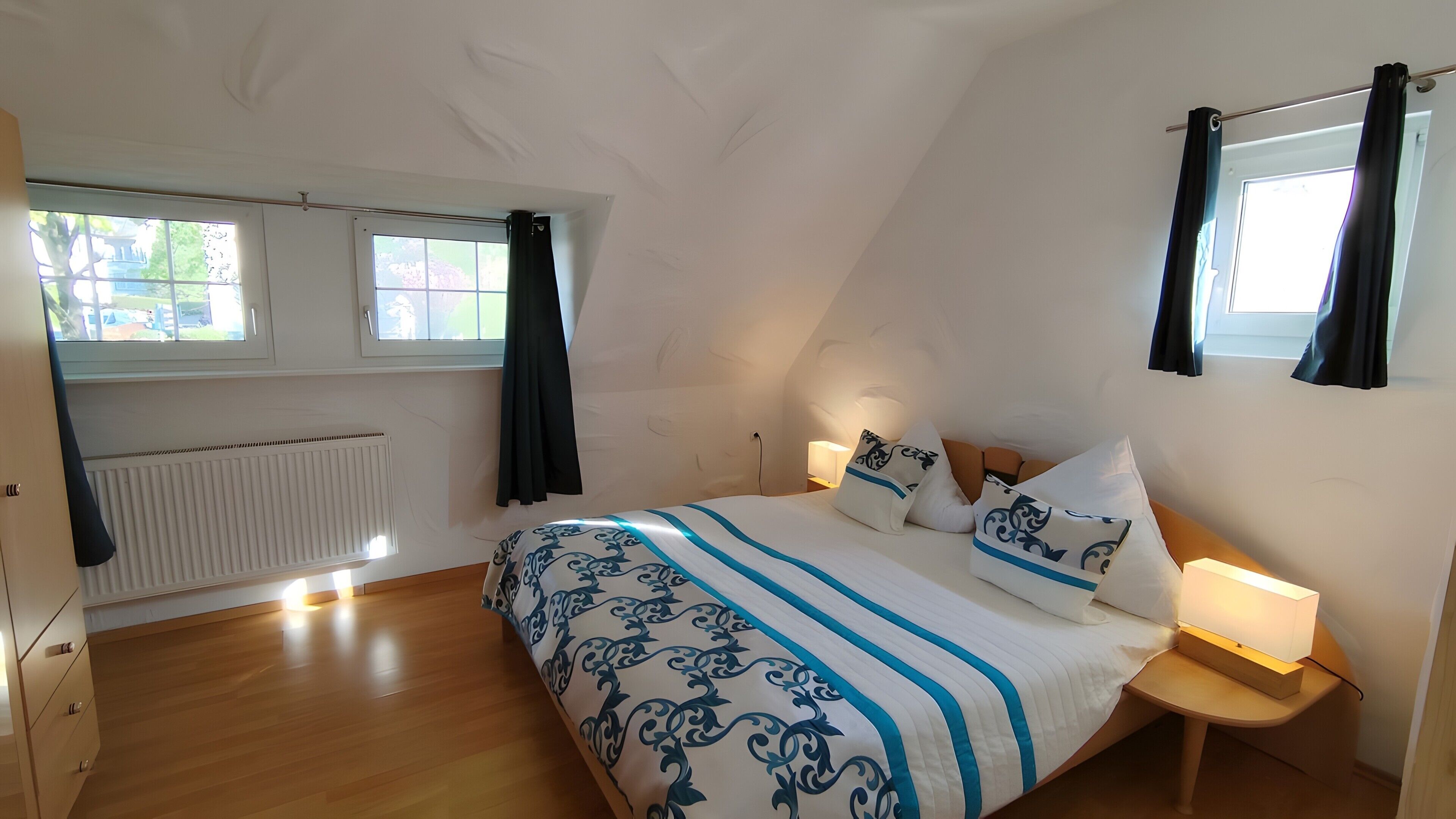 Ein Schlafzimmer mit einem Bett, einem Nachttisch mit Lampe, einem Fenster mit Vorhängen und einer Heizung.