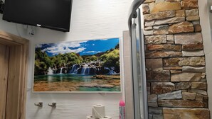 Un baño con pared de piedra, televisor montado y un cuadro de una cascada.