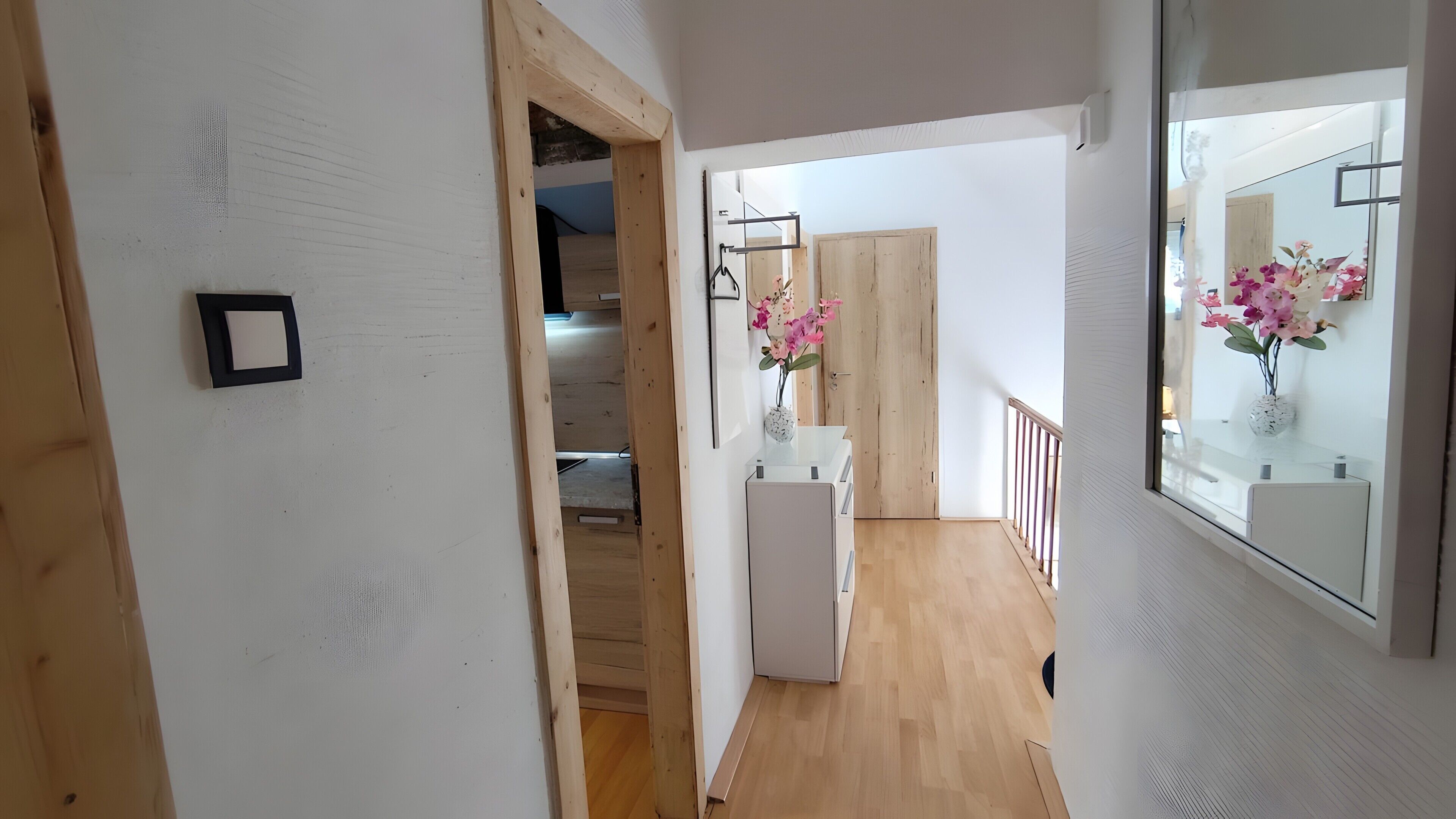 Kapea käytävä, jossa on puulattia, valkoinen ovi ja valkoinen seinä, jossa on taulunkehys.
