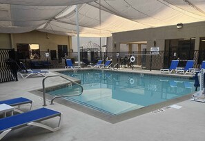 Ein Innenpool mit blauen Liegestühlen, einer Rettungswache und einem überdachten Bereich mit Netzabdeckung.