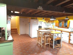 A kitchen with a central island, wooden beams, a refrigerator, and a microwave.