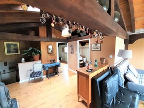 A rustic interior with a wooden ceiling, a sofa, a dining area, and a kitchen visible through an open doorway.