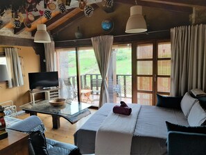 A room with a bed, a TV, a table, and a balcony with a view of the outdoors.