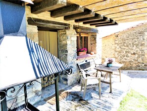 Un bâtiment en pierre doté d’un barbecue, d’un espace extérieur aménagé pour s’asseoir et d’un mur en pierre.