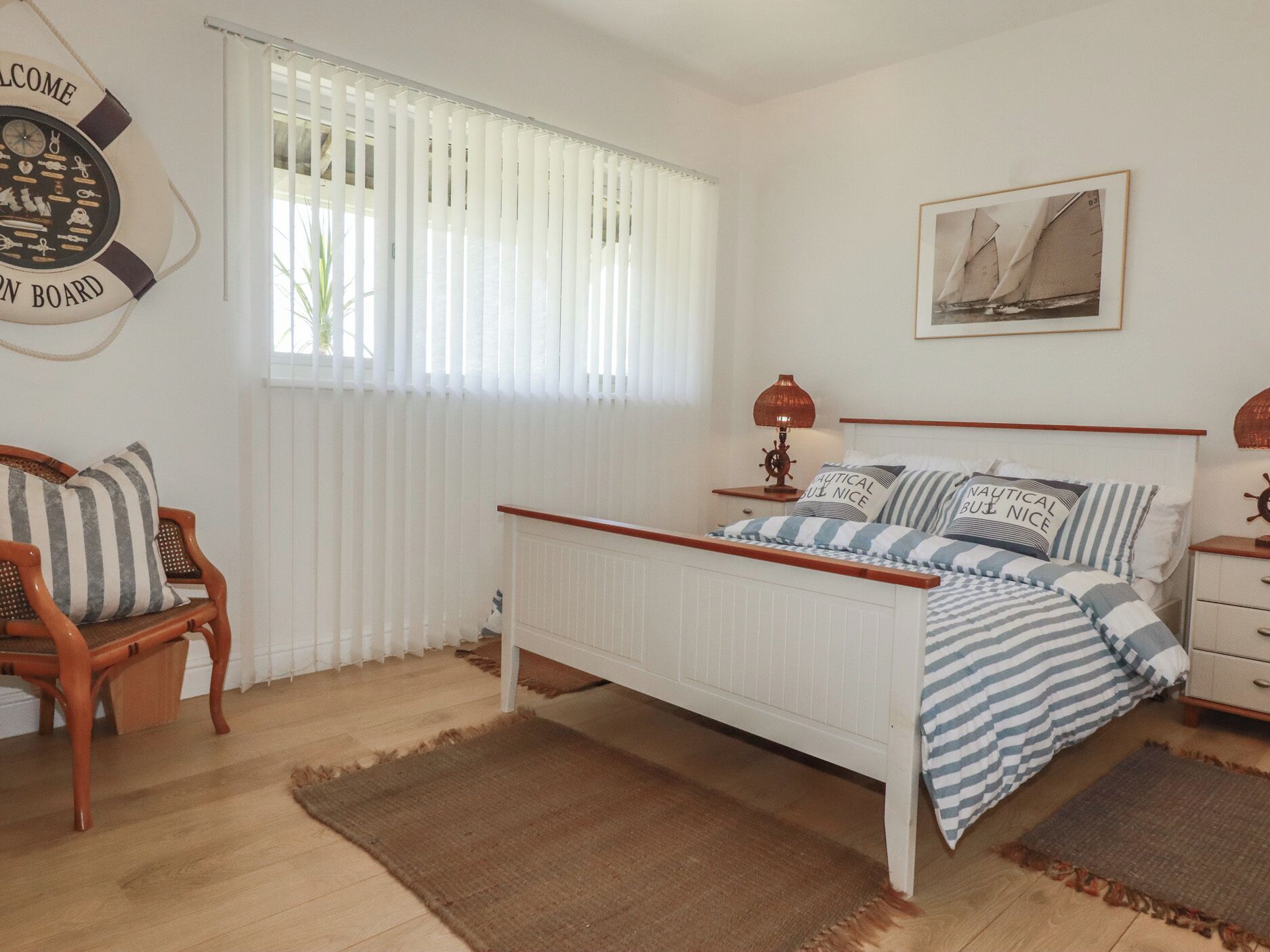 A bedroom with a bed, a nightstand, a lamp, a chair, a window with blinds, a wall clock, and a framed picture.
