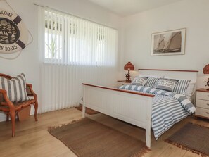 Une chambre à coucher comprenant un lit, une table de chevet, une lampe, une chaise, une fenêtre avec des stores, une horloge murale et un tableau encadré.