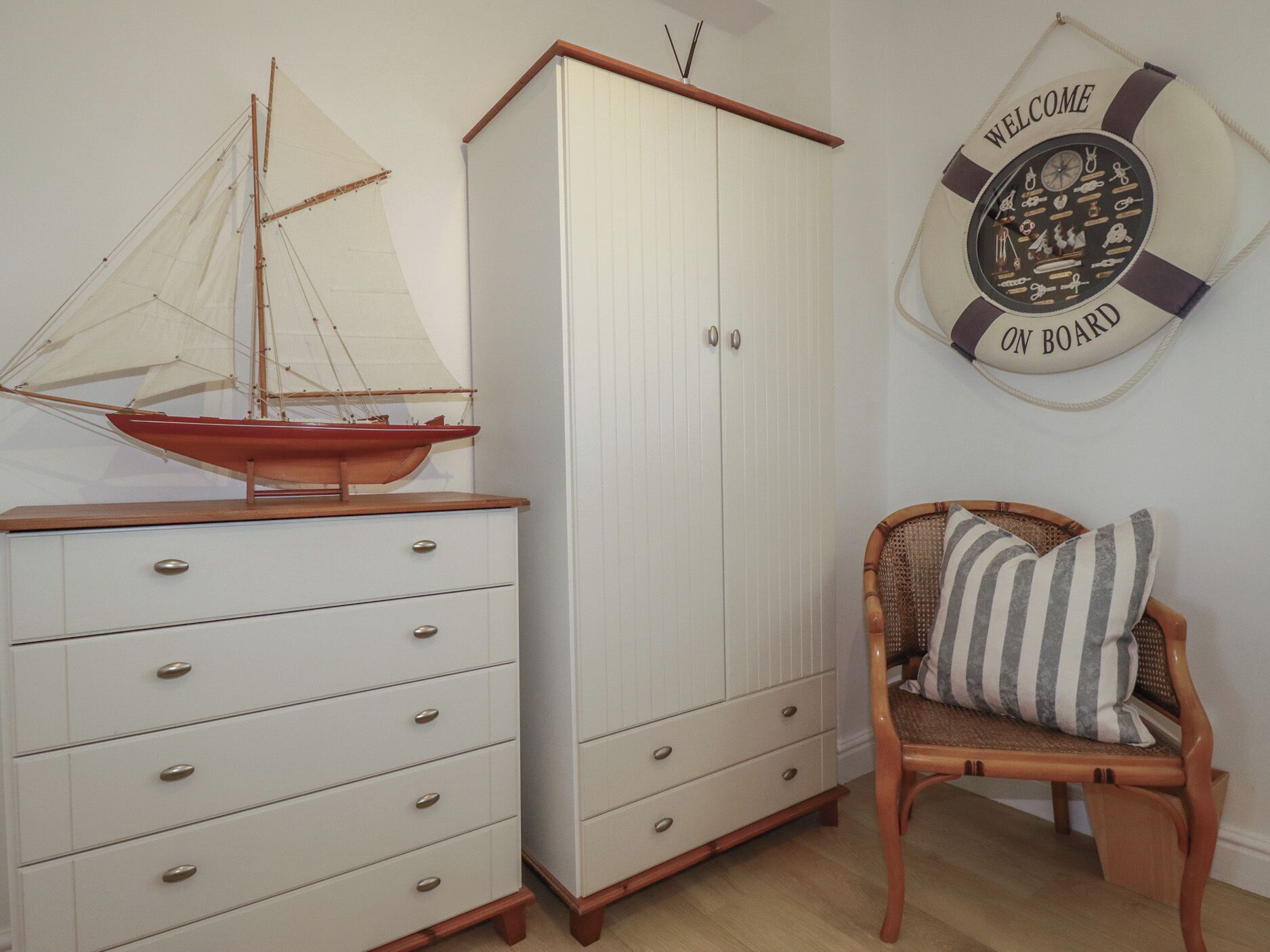 A room with a white wardrobe, a wooden chair with a striped cushion, and a wall decoration with 'WELCOME ON BOARD' text.