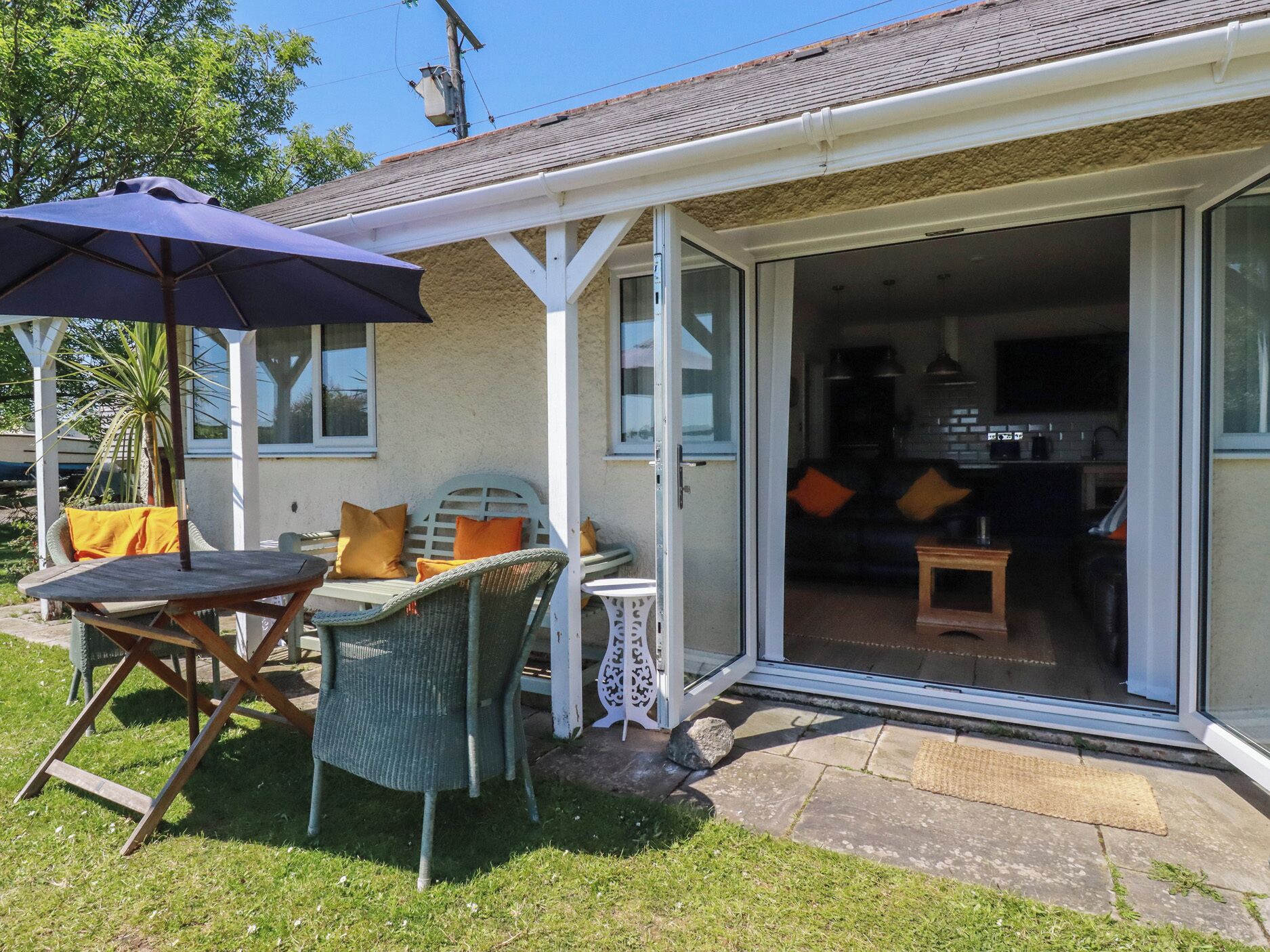A house with a patio, a table, chairs, an umbrella, and a sliding glass door leading to an interior with a sofa and a television.