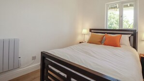 A bedroom with a bed, a window, a nightstand, and a wall-mounted heater. - Rollies Retreat (Fowey)