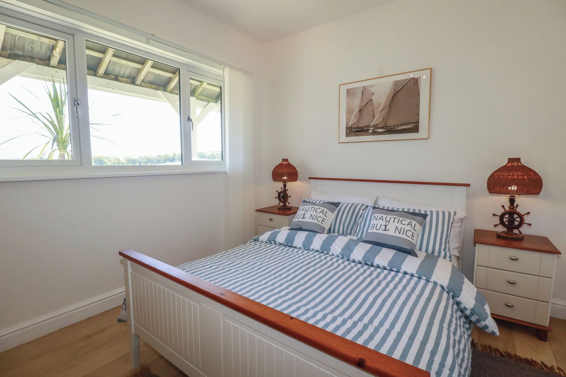 A bedroom with a bed, two nightstands, a window, a framed picture on the wall, and a wooden floor.