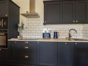 A kitchen with dark cabinets, a stainless steel sink, and a built-in oven. - Rollies Retreat (Fowey)
