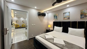 Une chambre d’hôtel équipée d’un lit, d’une table de chevet, d’une lampe, d’œuvres d’art et d’un ventilateur de plafond.