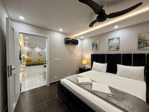 A hotel room with a bed, bedside table, lamp, artwork, and a ceiling fan. - 2 Bedroom - Tropical Suite Apartment by Lux Haven Stays - Central Lahore (Lahore)