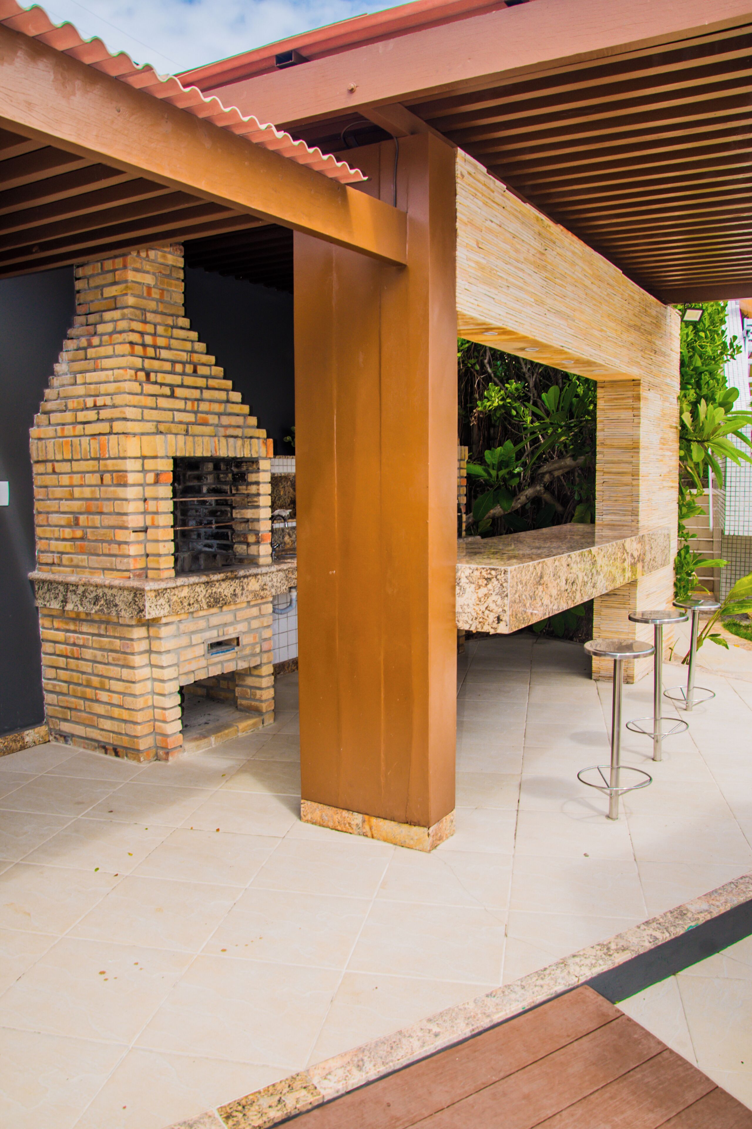 Un espace barbecue extérieur doté d’un four en briques, d’un coin salon couvert et d’une terrasse carrelée.