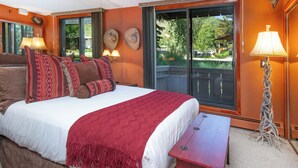 Una camera d'hotel con un letto grande, due lampade sui comodini, un comodino, una finestra con vista sugli alberi e un balcone.