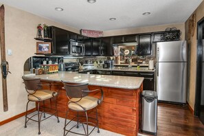 Una cocina con armarios oscuros, un refrigerador de acero inoxidable y una zona de bar con taburetes.