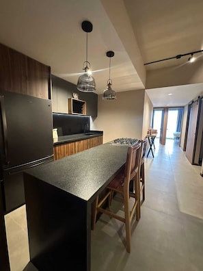 A modern kitchen with a central island, pendant lighting, and a dining area with wooden chairs. - Confortable Depa 2 BR A/C, Chapu, Gym, Cas y Expo (Guadalajara)