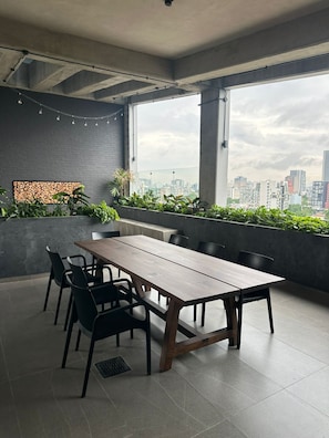 A modern meeting room with a long table, black chairs, a city view, and a brick wall with plants. - Confortable Depa 2 BR A/C, Chapu, Gym, Cas y Expo (Guadalajara)