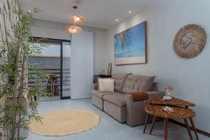 A modern living room with a sofa, a small wooden table, a large painting, and a bamboo plant. - TOCA GAMBOA - Apartment 190m from Patacho Beach on the Ecological Route of Miracles - AL (Porto de Pedras)