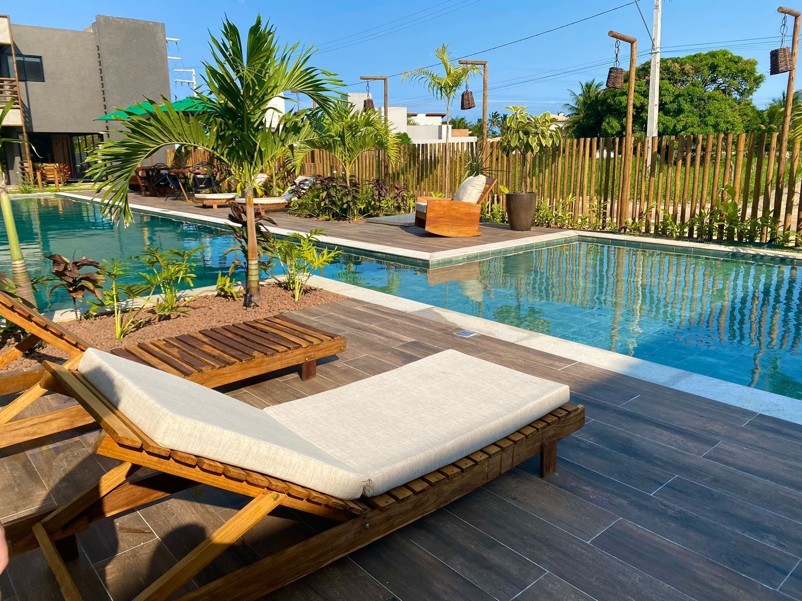 A pool area with wooden loungers, a small seating area, and a bamboo fence.