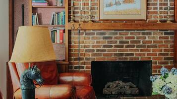 A cozy living room with a brick fireplace, leather sofa, a bookshelf, and a framed picture above the fireplace.