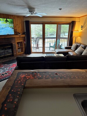 En stue med pejs, sofa, sofabord med lys, loftventilator og udsigt gennem et skydedør.