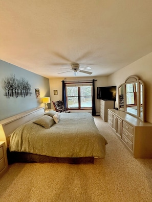A bedroom with a bed, a ceiling fan, a dresser, a TV, and a window with curtains.