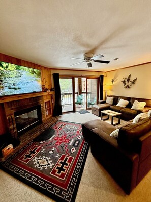 A living room with a fireplace, a large flat-screen TV, a leather sofa, and a patterned rug.