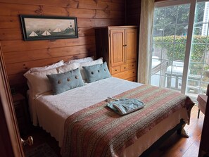 Un dormitorio con paneles de madera, una cama, almohadas, un cuadro enmarco y un armario de madera.