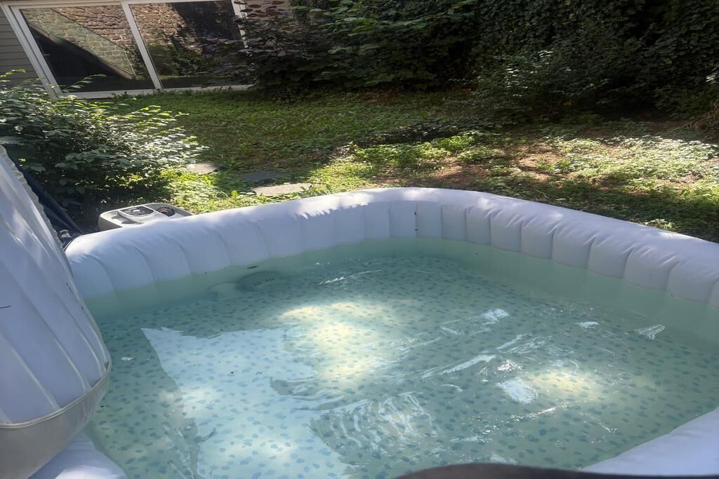 An inflatable hot tub in a backyard with a stone wall and greenery in the background.