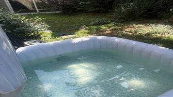 An inflatable hot tub in a backyard with a stone wall and greenery in the background.