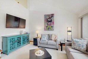 A living room with a sofa, a coffee table, a teal cabinet, a flat-screen TV, and a painting on the wall. - Baystrand II in Dewey Beach walk to beach (Dewey Beach)