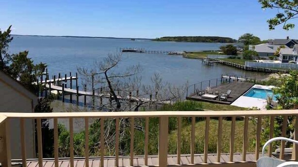 Une vue depuis un balcon donnant sur un lac, avec une jetée, une piscine et une maison en arrière-plan.