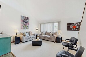 Un salon moderne avec deux canapés, une table basse, un fauteuil en cuir noir et des œuvres d’art accrochées aux murs.