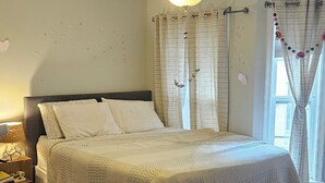 Ein Schlafzimmer mit einem Bett, Holzboden, Deckenventilator und Vorhängen.