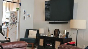 Ein Wohnzimmer mit Flachbildfernseher, Deckenventilator, Sofa, Couchtisch und einer Küche im Hintergrund.