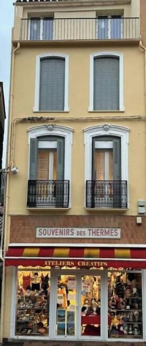 Ein zweistöckiges Gebäude mit einem Geschäft im Erdgeschoss namens 'SOUVENIRS des THERMES' und Balkonen im Obergeschoss.