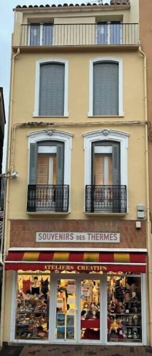 Ein zweistöckiges Gebäude mit einem Geschäft im Erdgeschoss namens 'SOUVENIRS des THERMES' und Balkonen im Obergeschoss.