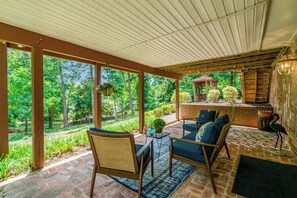 A covered patio with outdoor furniture, a brick wall, and a view of a garden. - Mount Vernon Hideaway-45 DAY Minimum Stay (Alexandria)