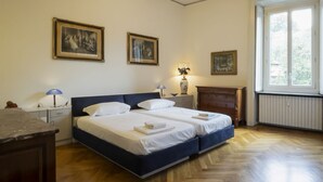 Ein Schlafzimmer mit zwei Betten, einem Nachttisch mit Lampen, einer Kommode und gerahmten Bildern an der Wand.