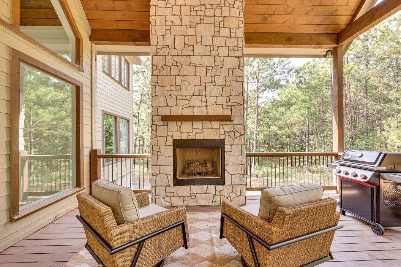 A covered outdoor area with stone walls, a fireplace, wicker furniture, and a grill.
