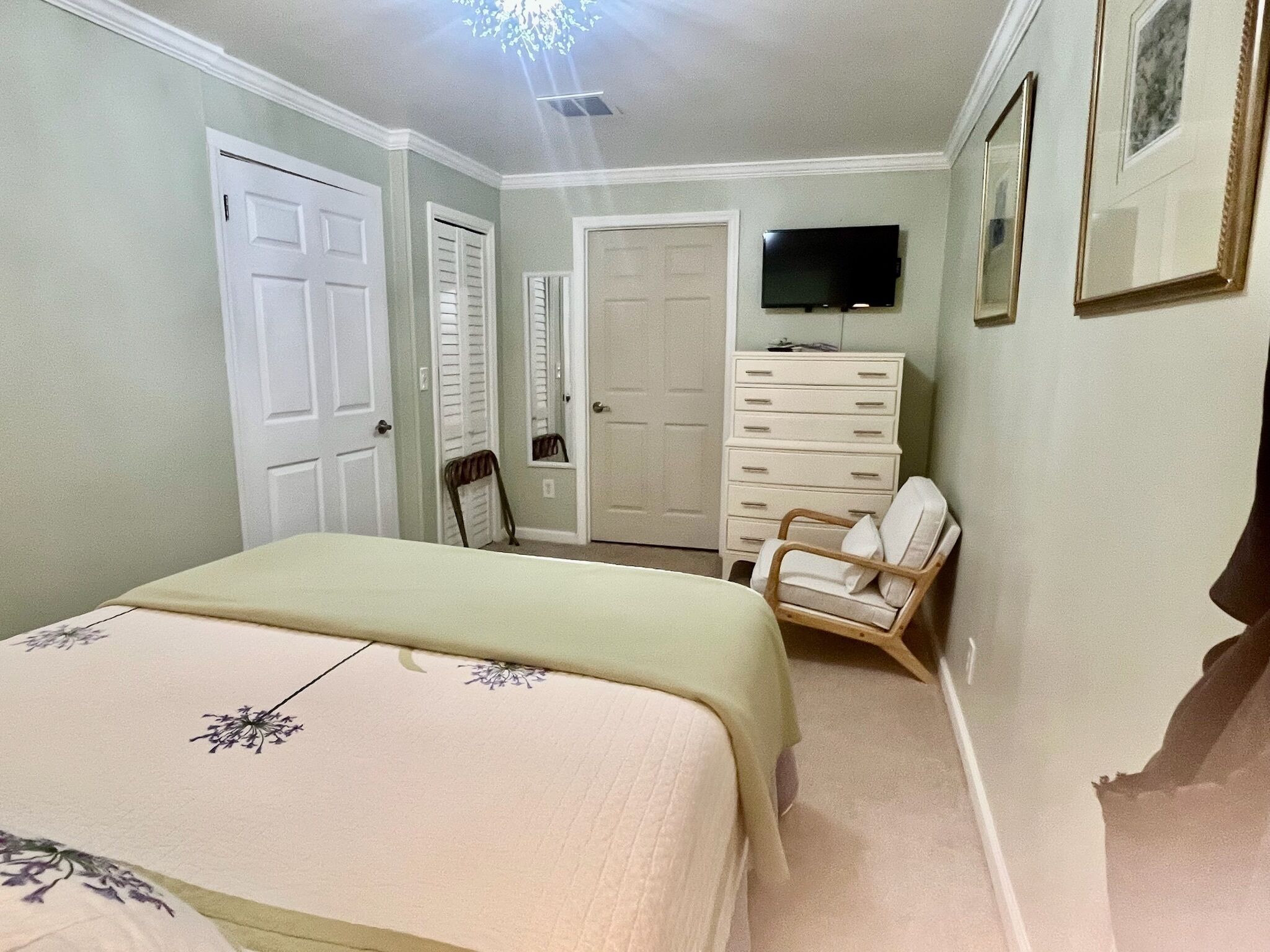 A bedroom with a bed, dresser, chair, and a TV on the wall.