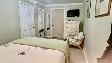 A bedroom with a bed, dresser, chair, and a TV on the wall.