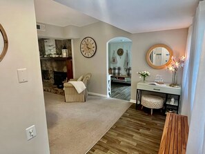 A living room with a fireplace, a clock, a mirror, and a small table with a vase.