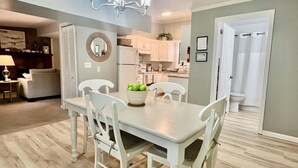 A dining area with a table, chairs, a bowl of fruit, and a kitchen in the background. - The Sanctuary in Warm Springs GA (Warm Springs)