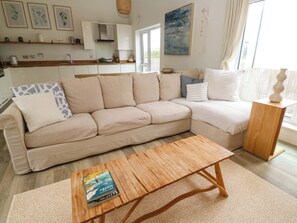 En stue med en beige sofa, et træbord og et køkken i baggrunden.