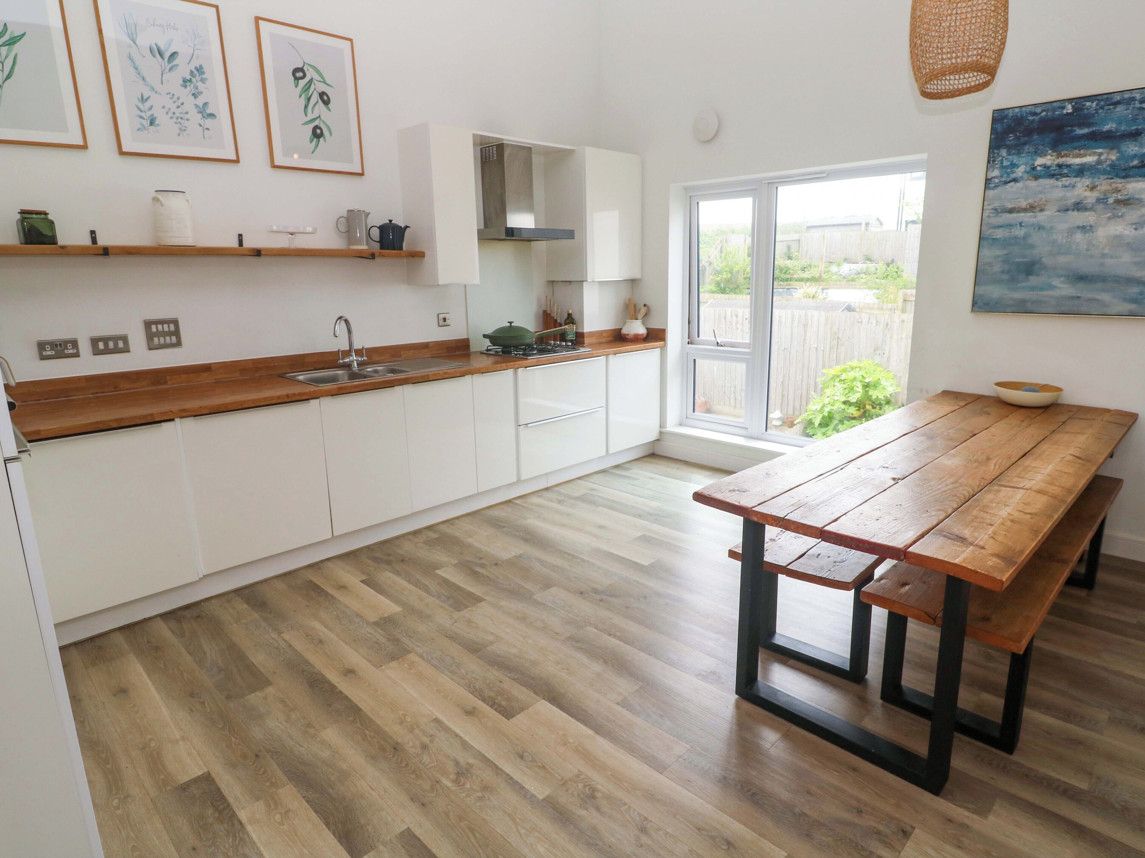 A modern kitchen with white cabinets, a wooden countertop, a sink, and a wooden dining table.