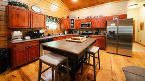 Een houten keuken in cottage-stijl, met houten kastjes, een centraal eiland met krukken, een roestvrijstalen koelkast en een magnetron.