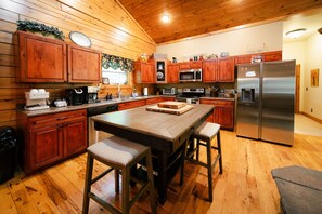 A wooden cabin-style kitchen with wooden cabinets, a central island with stools, a stainless steel refrigerator, and a microwave. - Big Rock | Theater Room, Hot Tub, Hocking Hills (Rockbridge)